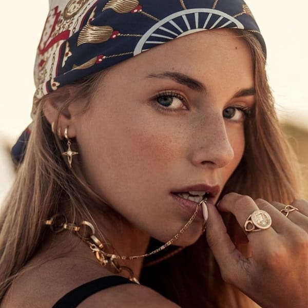 Mujer con accesorios de oro y pañuelo en la cabeza.