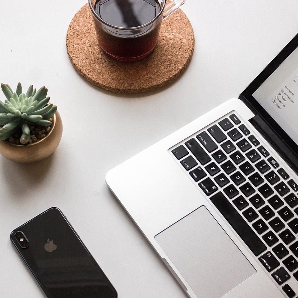 Escritorio con portátil, teléfono, planta y bebida.